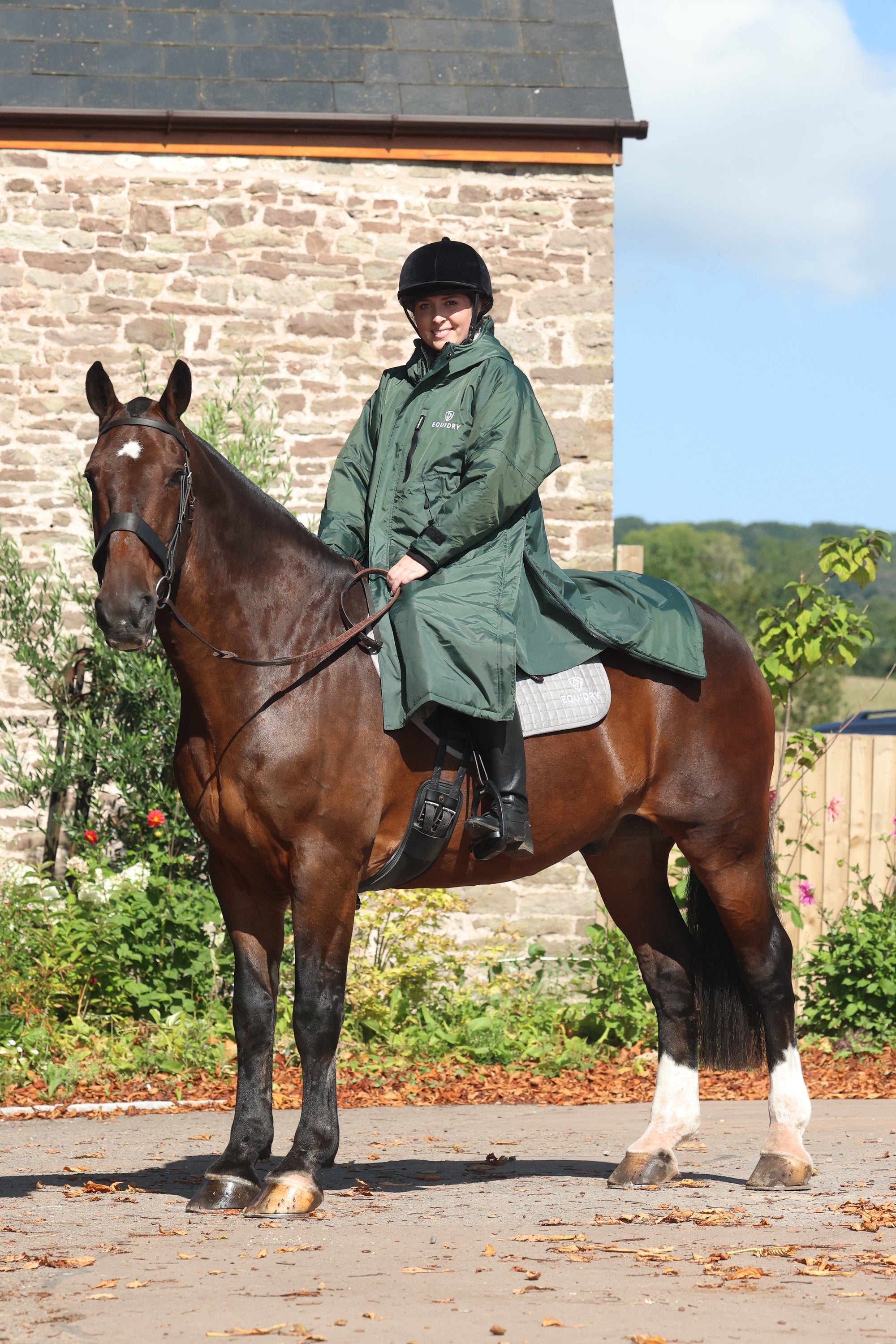 EQUIDRY women's long waterproof horse riding coat in black forest green/cream modelled by rider out hacking on horse showing storm skirts 