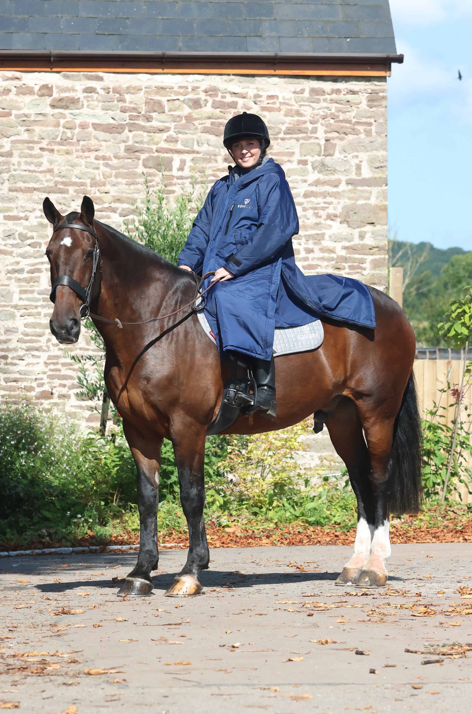EQUIDRY women's long waterproof horse riding coat in navy/charcoal modelled by rider on horseback 