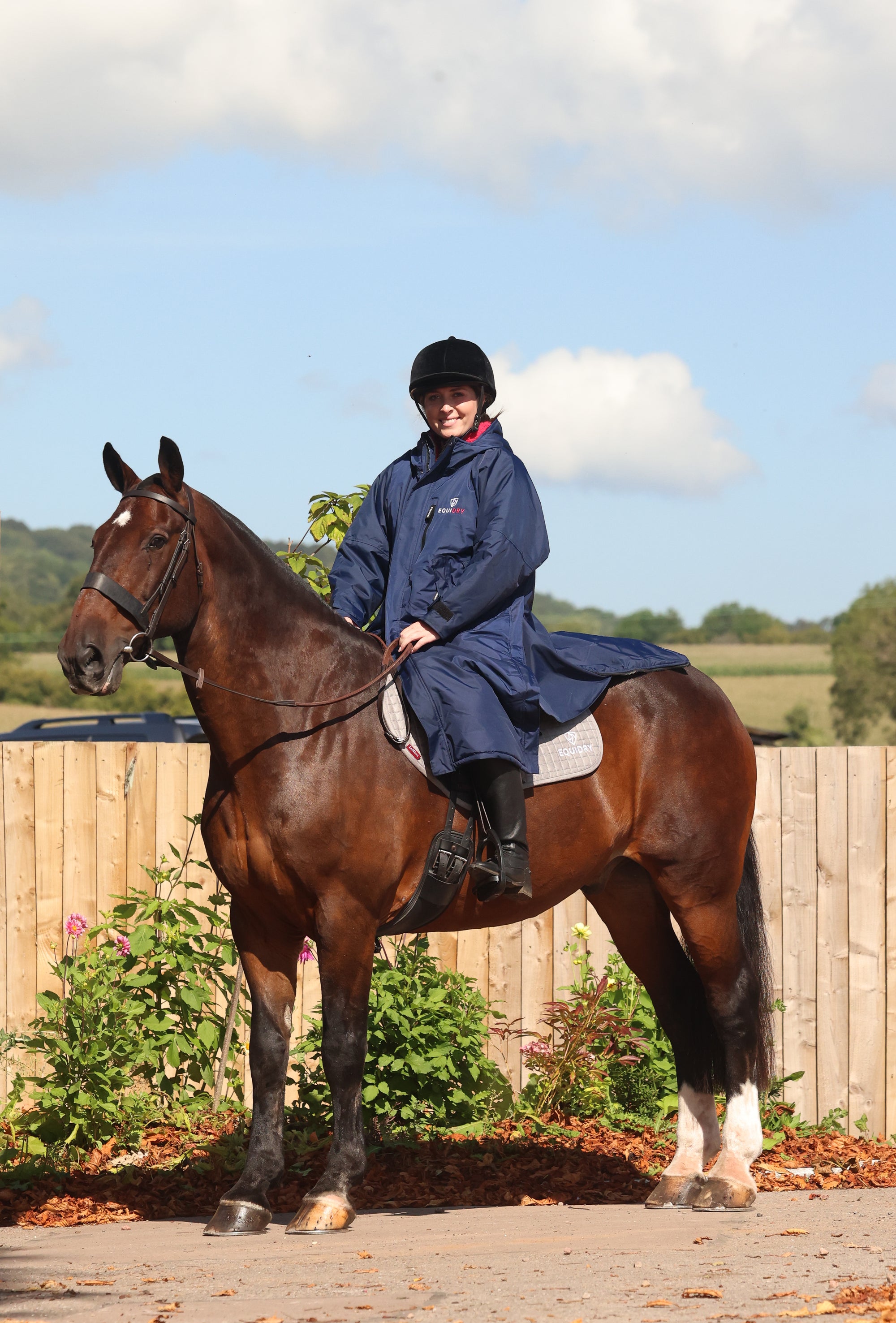 EQUIDRY women's long waterproof horse riding coat in navy/raspberry modelled by rider on horse showing storm skirts 