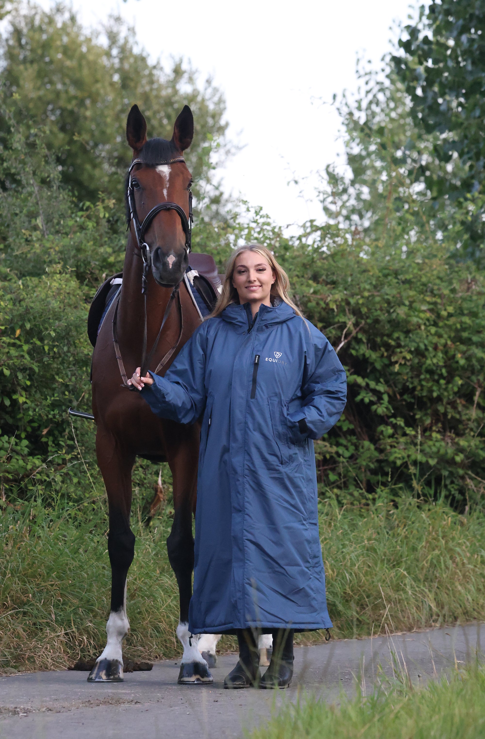 EQUIDRY women's long waterproof horse riding coat in steel blue/charcoal modelled by rider with horse