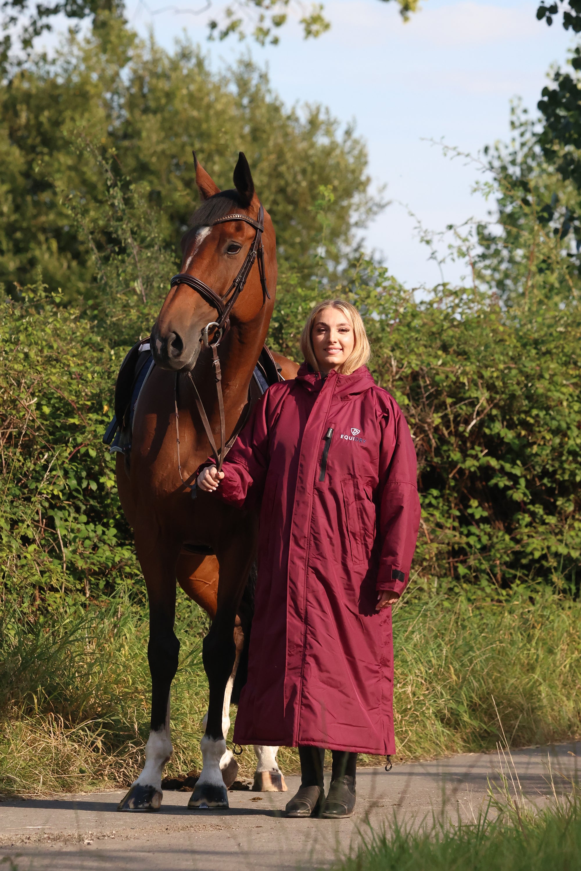 EQUIDRY women's long waterproof horse riding coat in plum/navy worn by rider with horse