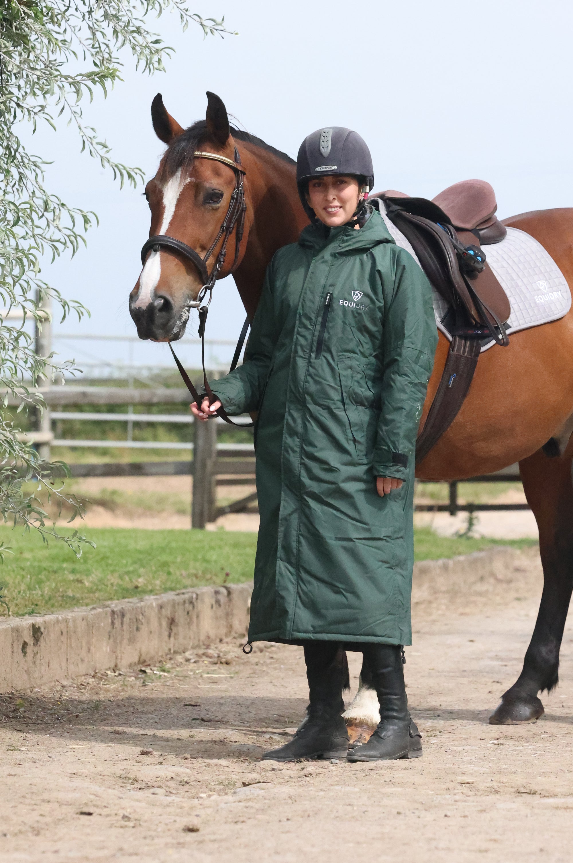 EQUIDRY women's long waterproof horse riding coat in black forest green/green shown by rider stood with horse