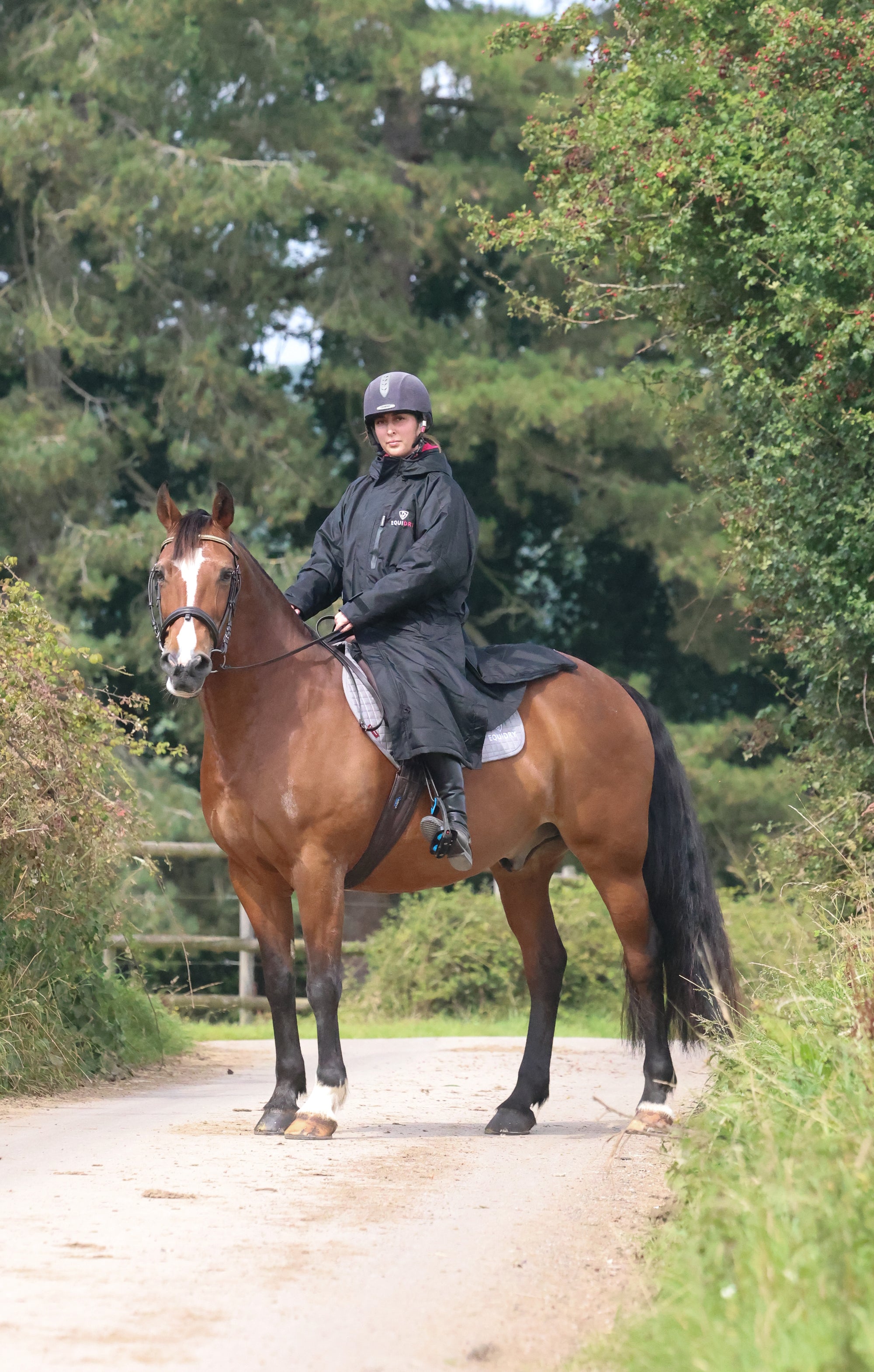 EQUIDRY women's long waterproof horse riding coat in black/peacock pink shown by rider out hacking on horse