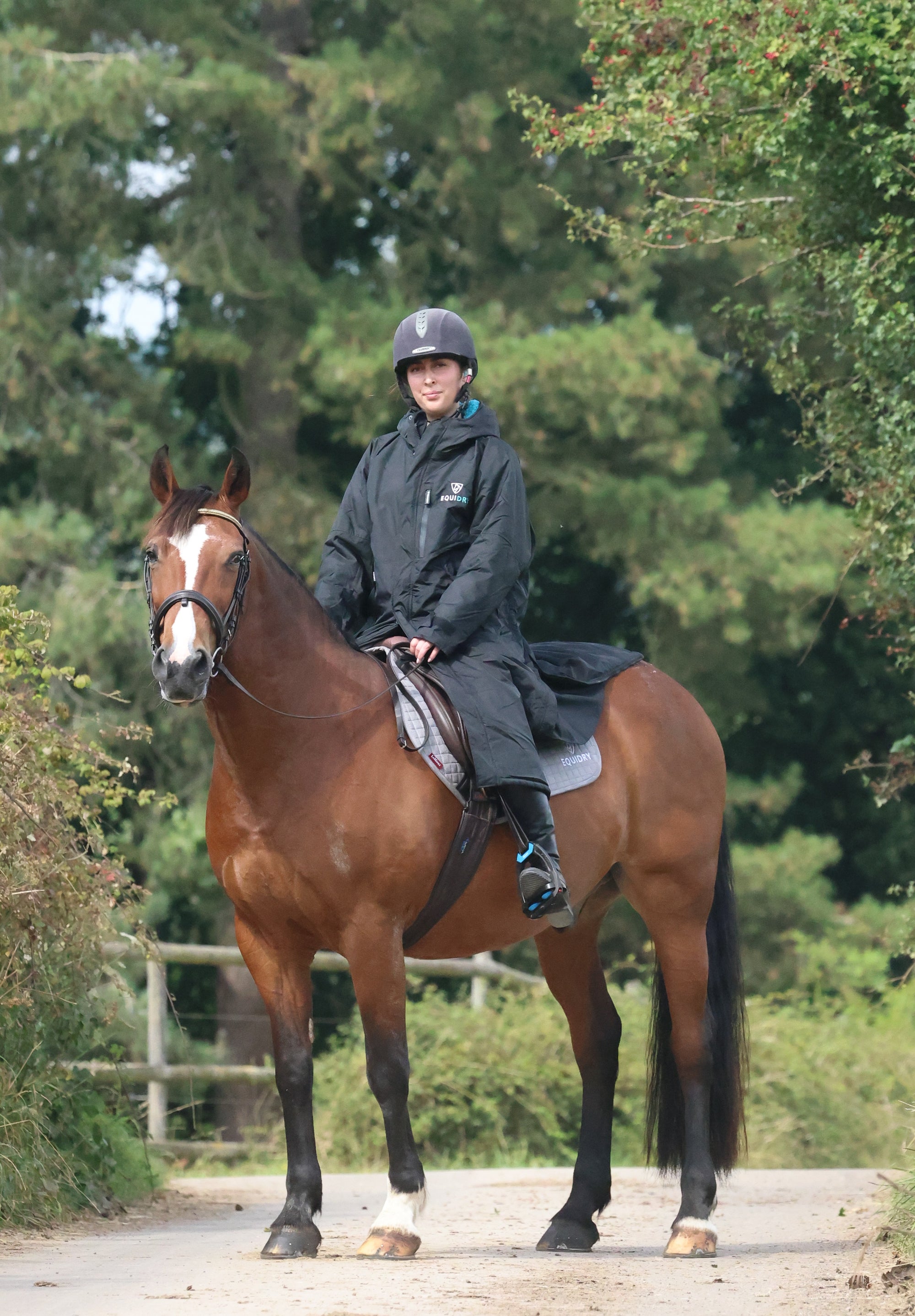 EQUIDRY women's long waterproof horse riding coat in black/turquoise modelled by rider hacking on horse