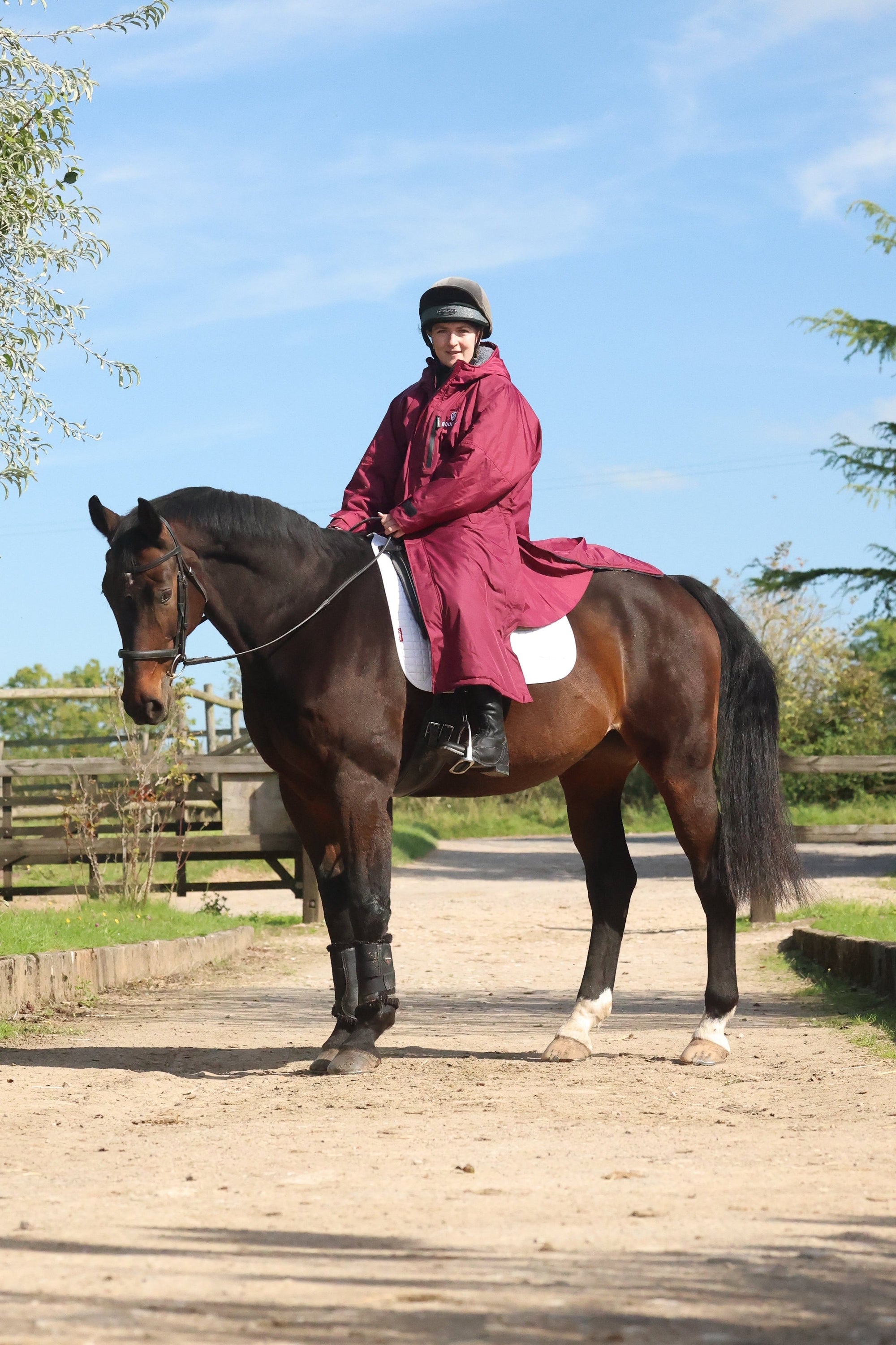 EQUIDRY women's long waterproof horse riding coat in plum/charcoal worn by on horse showing storm skirts and side zips