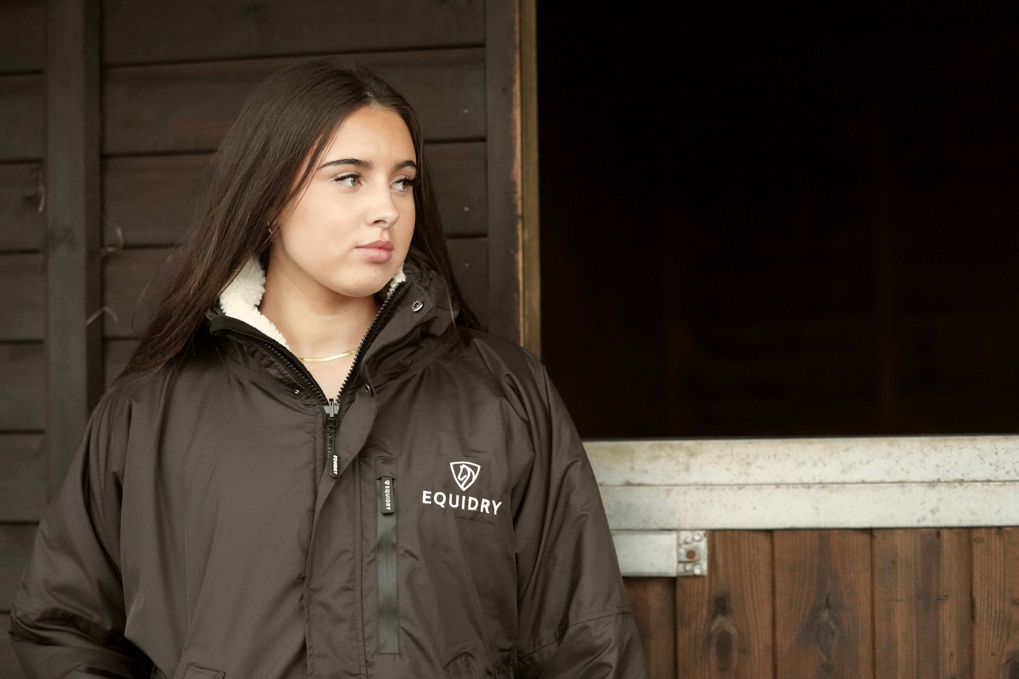 EQUIDRY women's long waterproof horse riding coat in rich brown/cream shown being worn on the yard