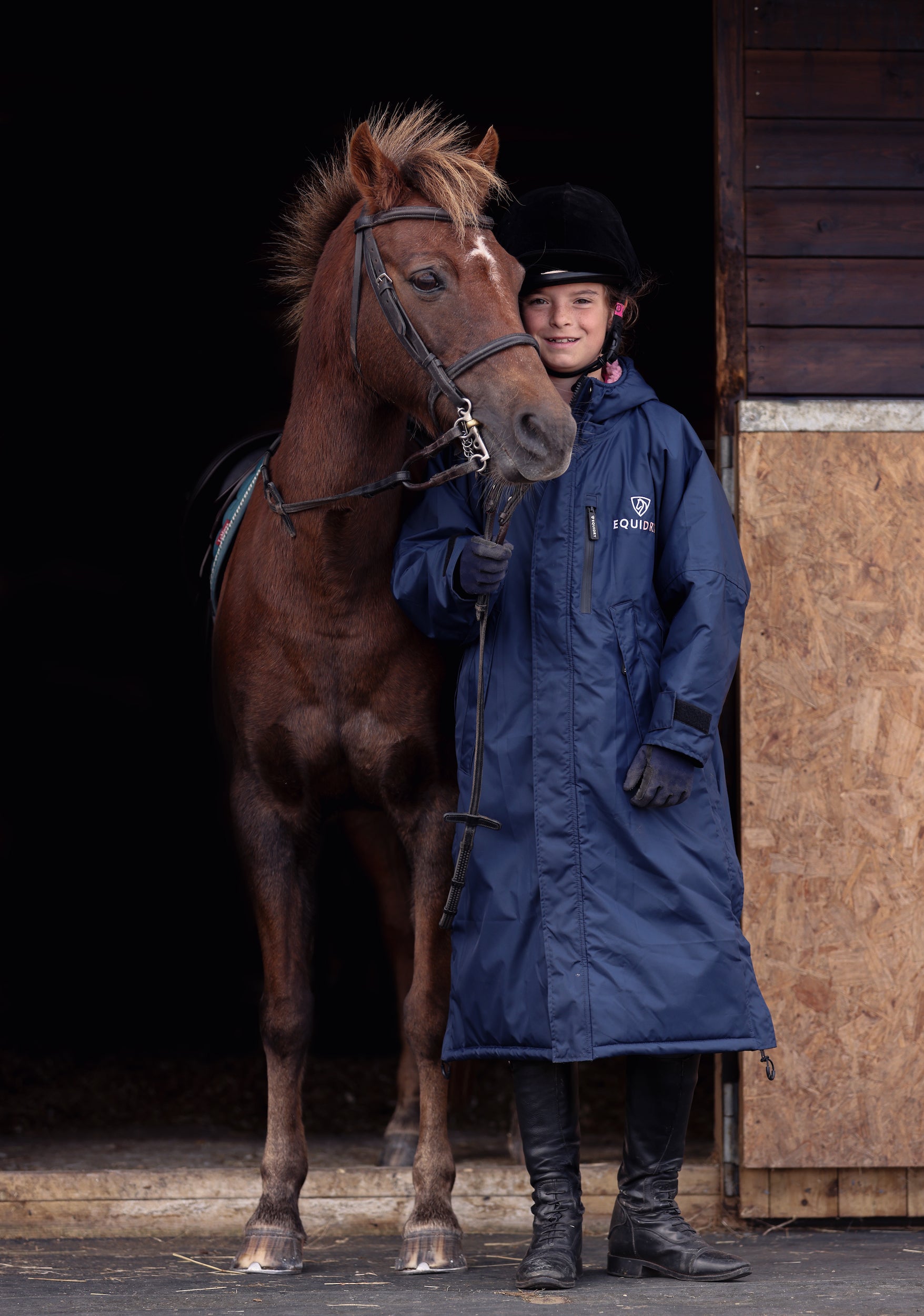 EQUIDRY women's long waterproof horse riding coat in navy/pale pink modelled by young girl with horse in stable 