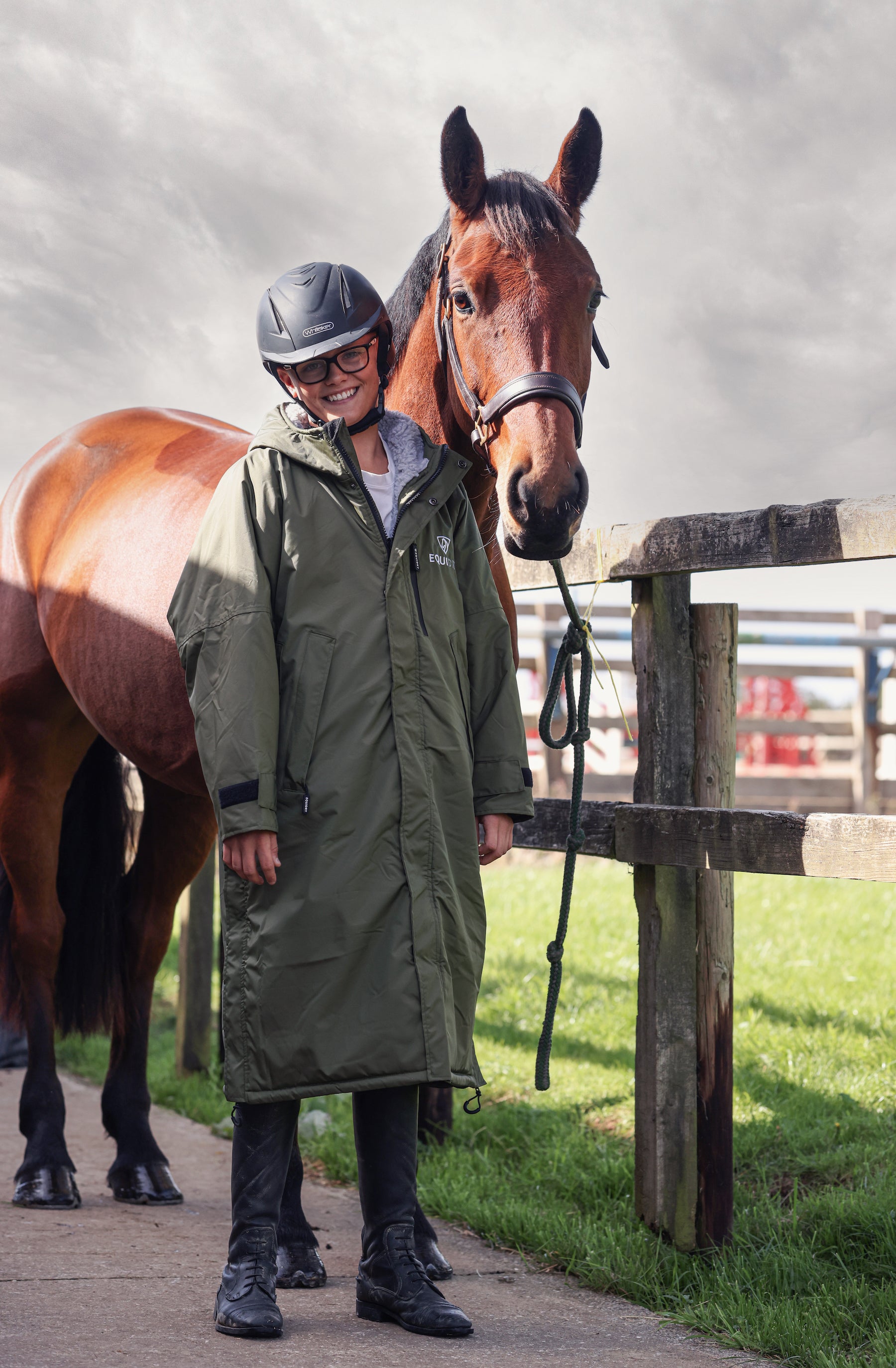 EQUIDRY men's long waterproof horse riding coat in Dark Olive/Grey modelled by rider with horse on yard 