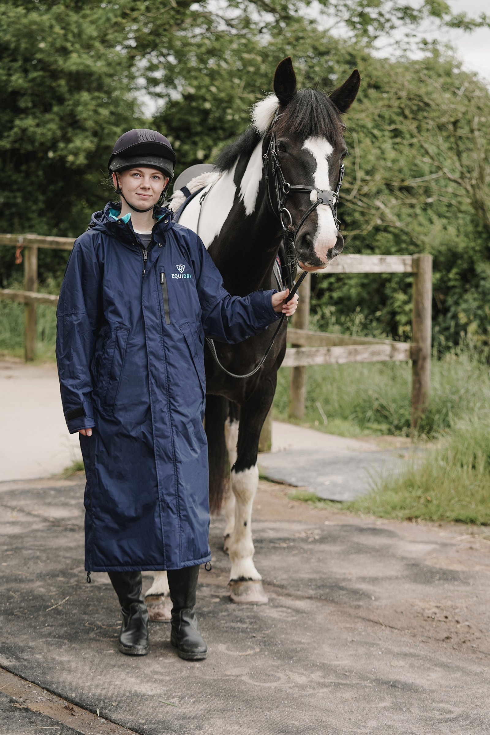 EQUIDRY women's thin fleece stowaway hood long waterproof horse riding coat in navy/turquoise stood with horse